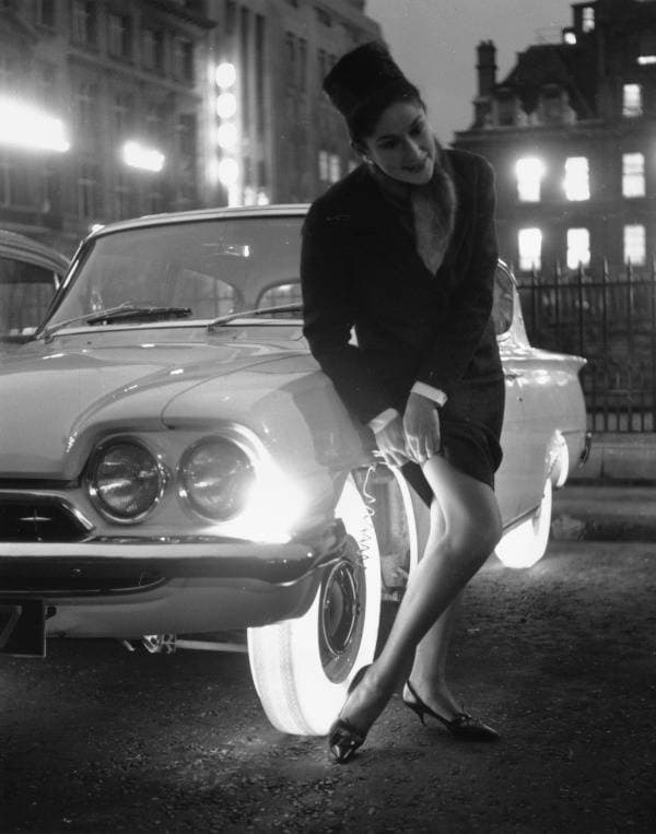 امرأة تقوم بتعديل جواربها الطويلة بجوار الإطارات المضيئة المصنعة من قبل شركة Goodyear عام 1961