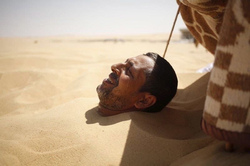 مريض يسترخي تحت أشعة الشمس اللاذعة والرمال الحارة