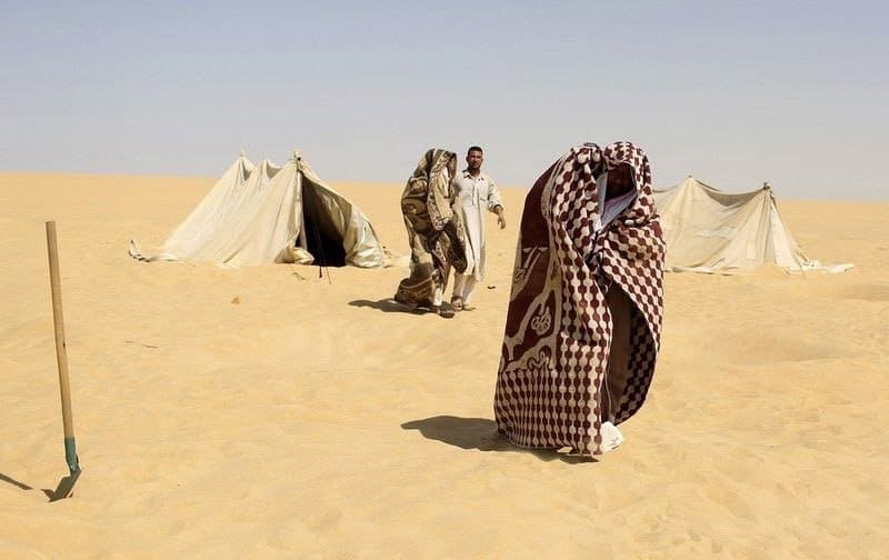 عامل يساعد المرضى الذين التحفوا ملاءات على مغادرة خيمة السونا بعد حماماتهم الرملية في (سيوا) بمصر.