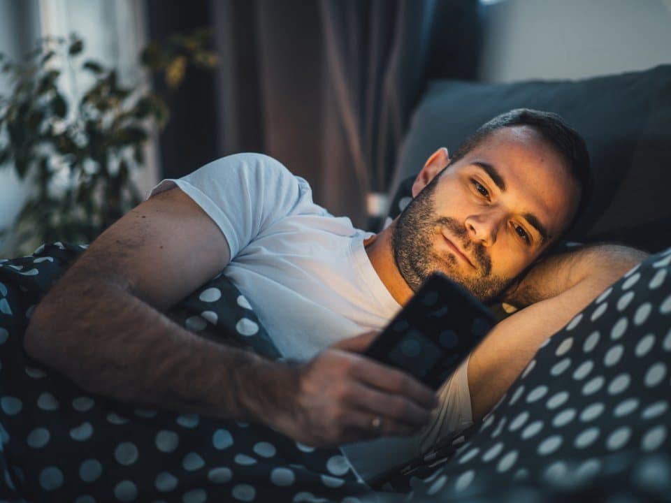 شخص مستلق على الفراش يتصفح هاتفه الذكي