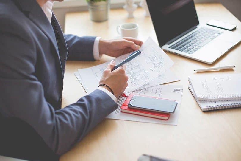شخص يجلس على طاولة بها أوراق وكناشة وهاتف ذكي