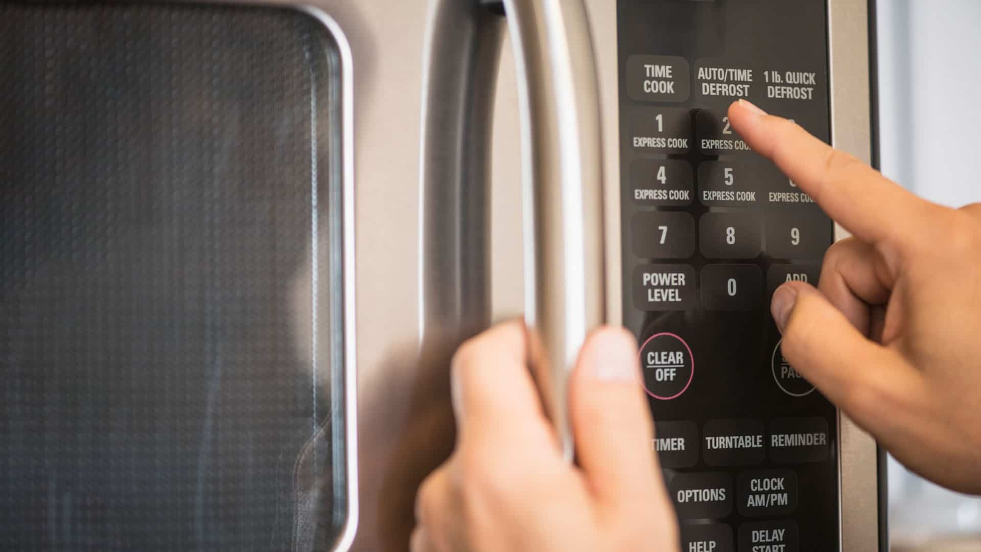 يد شخص تضغط على أزرار لوحة تحكم فرن الميكروويف