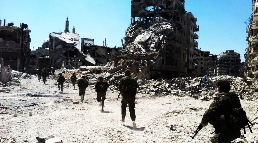 جنود سوريون يمشون بين مباني متهدمة