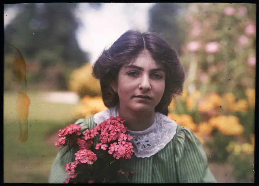 أوتوكروم لإبنة ”إثالدريدا جانيت لانغ“ في حديقة وهي تحمل باقة من الأزهار ذات لون زهري فاقع، سنة 1908