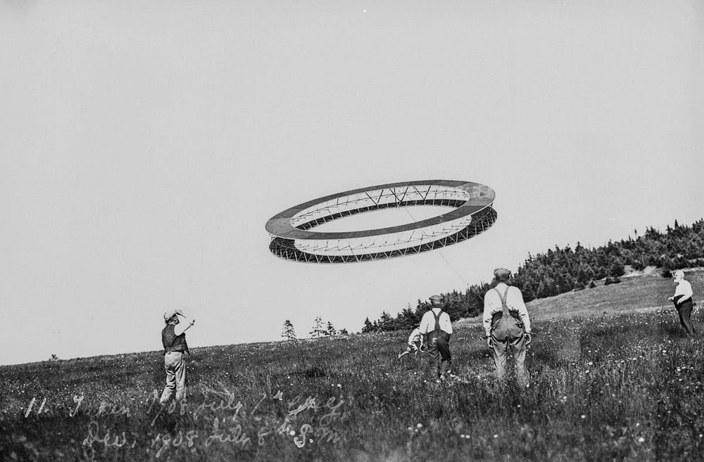 طائرات غراهام بيل الورقية رباعية السطوح: غراهام بيل على اليمين، ومساعده على اليسار يلاحظان طيران طائرة رباعية الأسطح دائرية الشكل في السابع من شهر يوليو 1908
