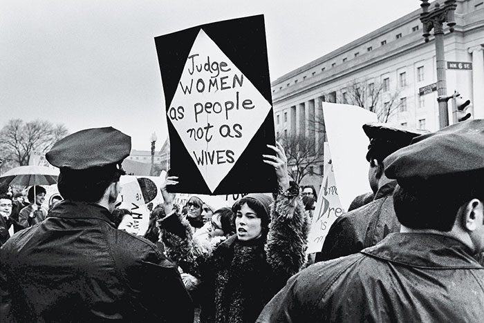 فتاة أمريكية ترفع لافتة خلال احتجاجها، لأجل حقوق المرأة، أمام مقر لجنة التجارة الاتحادي في (واشنطن – الولايات المتحدة الأمريكية)، تحت نظر رجال الشرطة خلال مراسيم تنصيب (ريتشارد نيكسون) Richard Nixon، في كانون الثاني/يناير 1969.