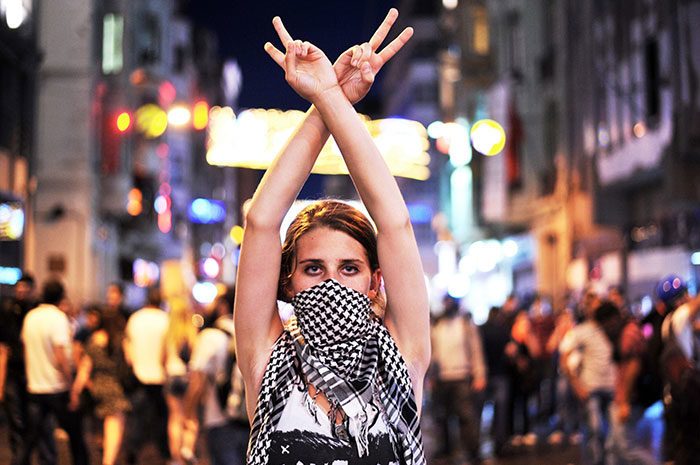 محتجة ضد الحكومة ترفع إشارة النصر خلال مناوشات بين المحتجين ورجال شرطة مكافحة الشغب في ساحة (تقسيم) Taksim في اسطنبول في تركيا، بتاريخ 22 حزيران/يونيو 2013.