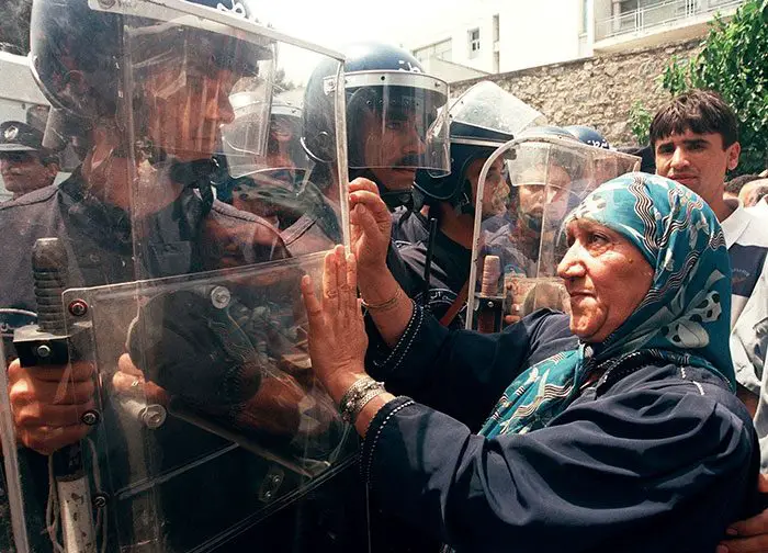 امرأة تومئ لشرطة مكافحة الشغب خلال احتجاج مُنَظَّم من قبل حزب التجمع من أجل الثقافة والديمقراطية (RCD)، في  الجزائر العاصمة، في 2 تموز/يوليو 1998.
