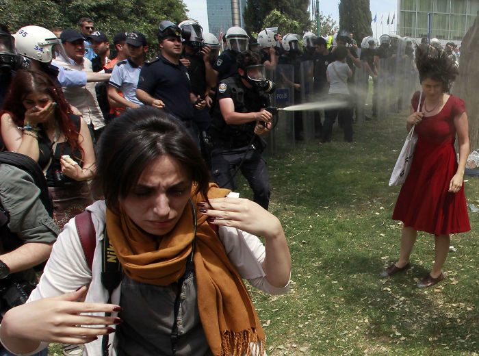 شرطي مكافحة شغب تركي يستخدم الغاز المسيل للدموع ضد محتجين على قرار إزالة أشجار من إحدى الحدائق بهدف توسيع طريق المشاة،= في ساحة (تقسيم) Taksim في اسطنبول، بتاريخ 28 أيار/مايو 2013.