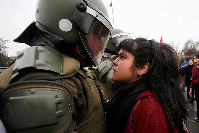 متظاهرة تواجه أحد عناصر شرطة مكافحة الشغب خلال إحدى تظاهرات الديمقراطية الأولى في (سانتياغو – تشيلي)، في 11 أيلول/سبتمبر 2016.