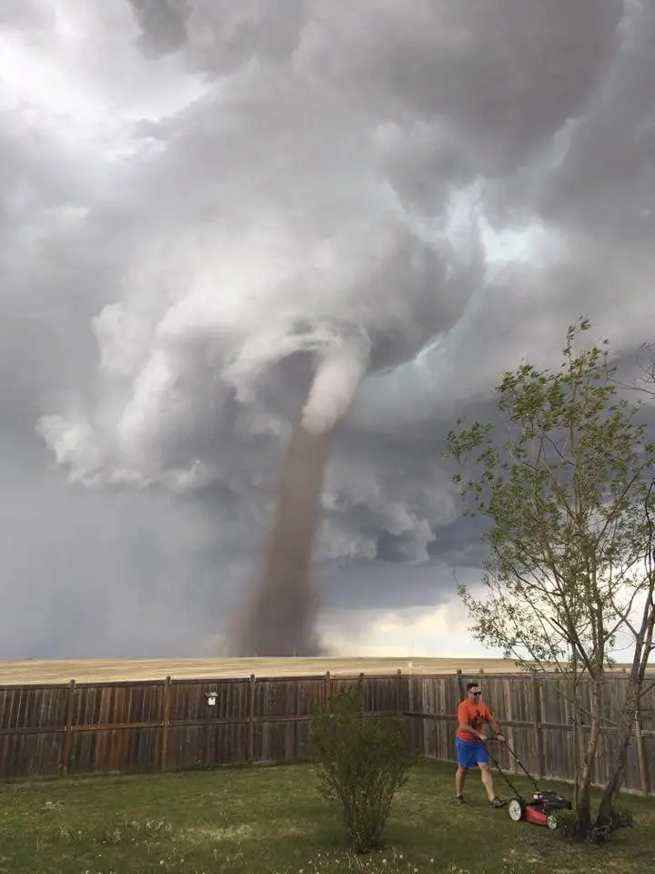 رجل يجز عشب حديقته بينما يقترب إعصار