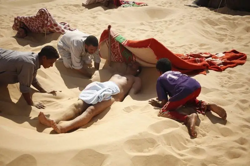 عمال يتعاونون على دفن أحد المرضى في الرمال الحارة خلال حمام الرمال الساخنة الخاص به في (سيوا) بمصر.