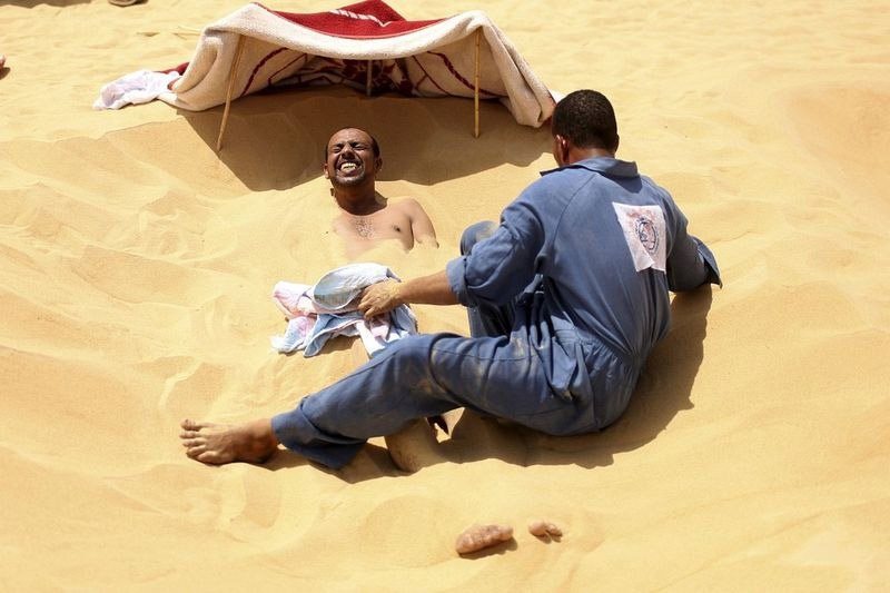 مريض يكشر لدى تغطية أحد العمال لجسده بواسطة الرمال الحارة في (سيوا) بمصر.