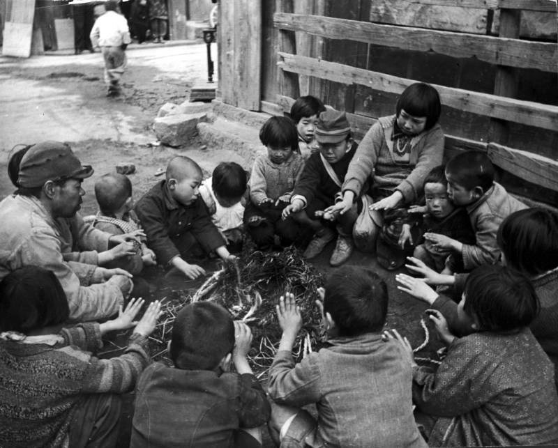 صورة لمجموعة من الأطفال والكبار المشردين وهم مجتمعون حول نار أشعلوها ليدفئوا أيديهم على أطراف مدينة (هيروشيما).