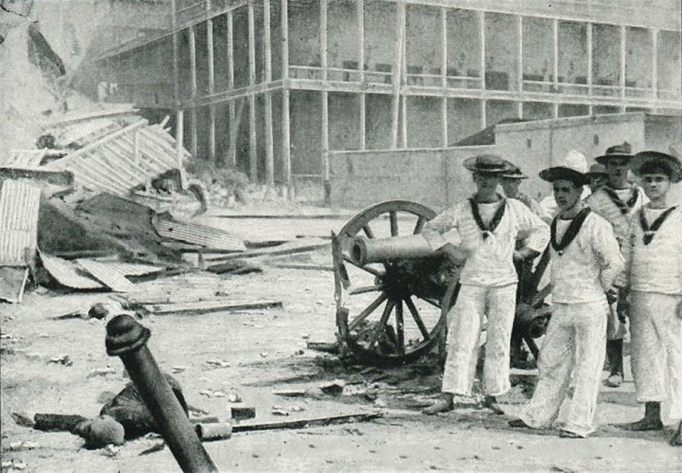 جنود البحرية الملكية البريطانية يقفون بالقرب من مدفع مدمر بجانب قصر السلطان في (زنجيبار) في سنة 1896، بعد الحرب الإنجليزية-الزنجيبارية.