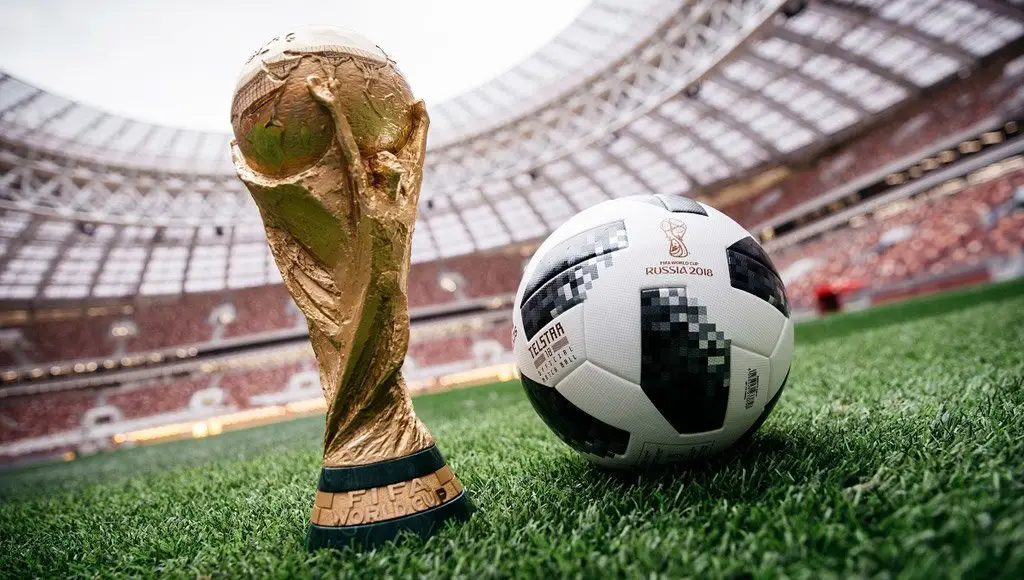 كأس العالم بجانبها كرة موضوعتان فوق أرضية ملعب