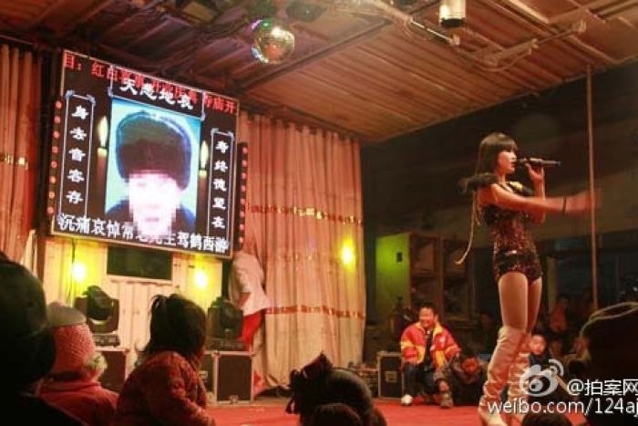 إحدى راقصات التعري في جنازة وخلفها صورة المتوفي والتي تحمل عبارات العزاء في الصين