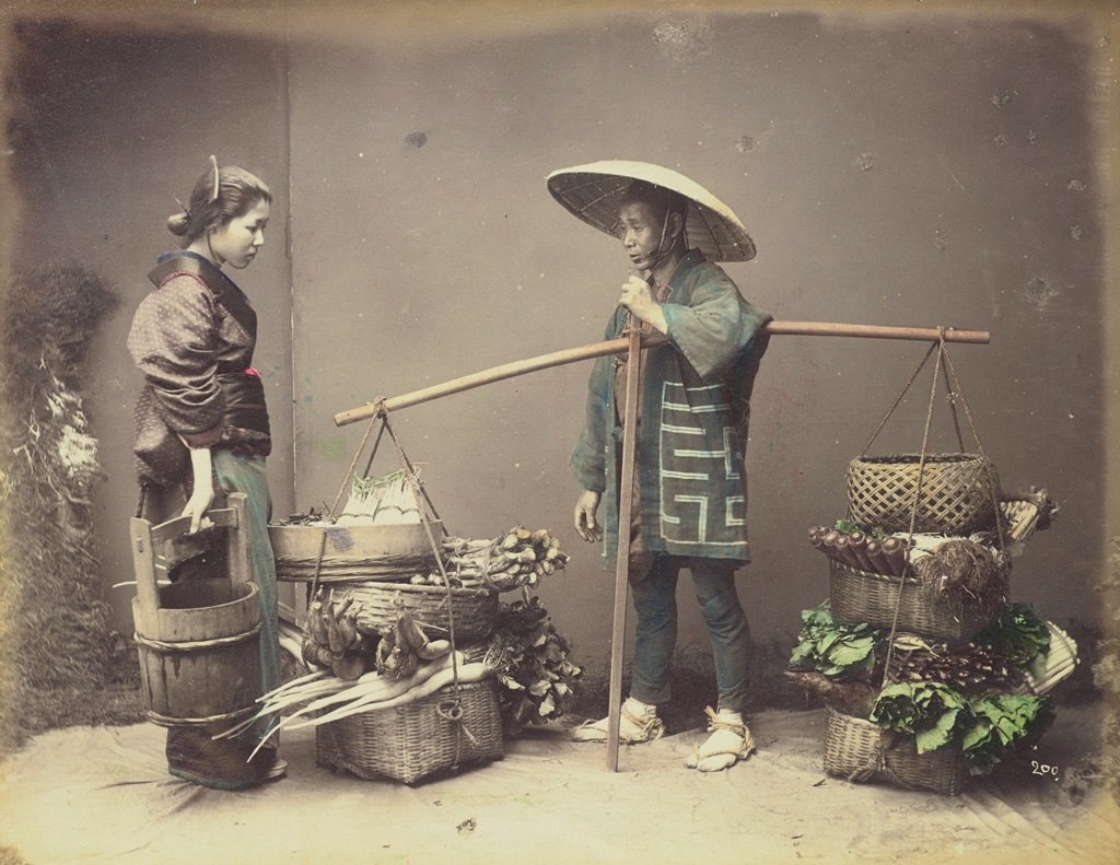 بائع خضار متجول يظهر ما لديه من بضاعة لإحدى الزبونات حوالي سنة 1880