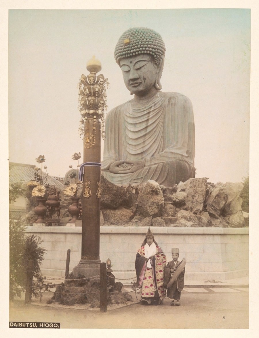 يقف اثنان من رجال الدين أمام تمثال بوذا الذي يسمى باللغة اليابانية (دايبوتسو) في مدينة (كوبيشي) حوالي سنة 1890