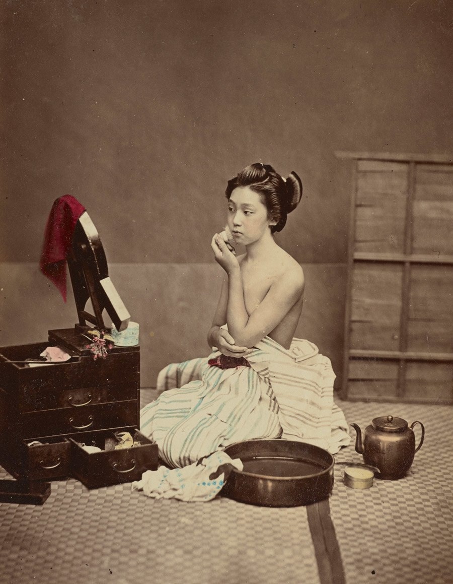 امرأة يابانية تضع مساحيق التجميل وتستعد ليومها، يوجد حوض من الماء على الأرض بجوارها. بين عامي 1870 و1900