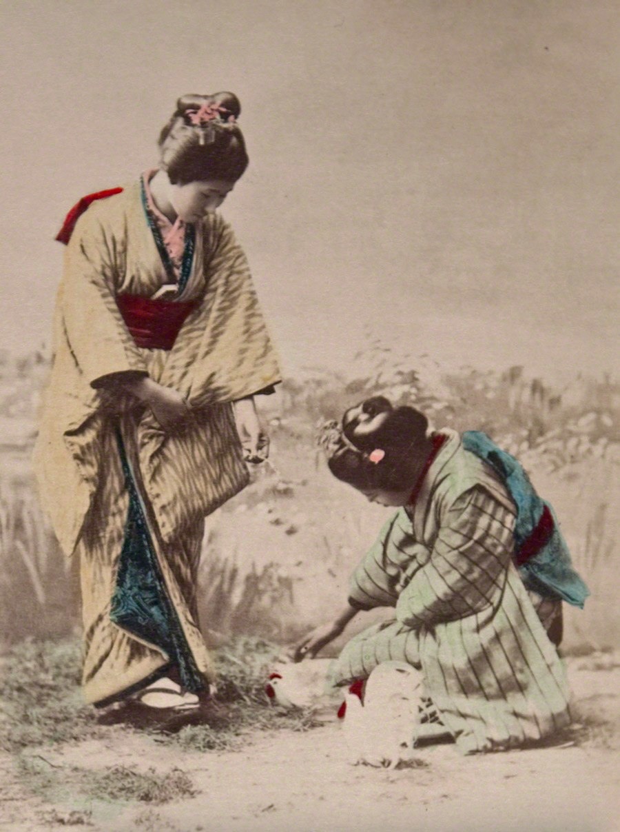 اثنين من النساء من الطبقة الثرية تنحنيان لإطعام بعض الدجاجات حوالي عام 1890