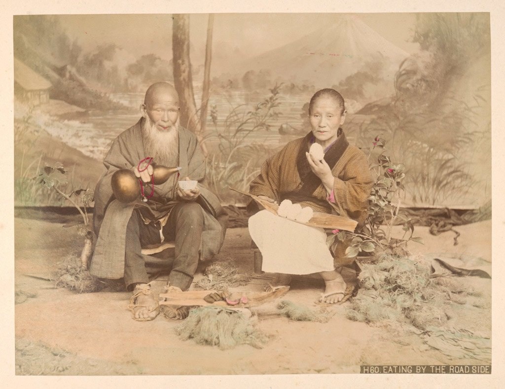 زوجان مسنان يجلسان أمام خلفية مرسومة يمثلان مشهدا كأنهما جالسان على جانب الطريق لأخذ قسط من الراحة وتناول بعض الطعام حوالي 1890