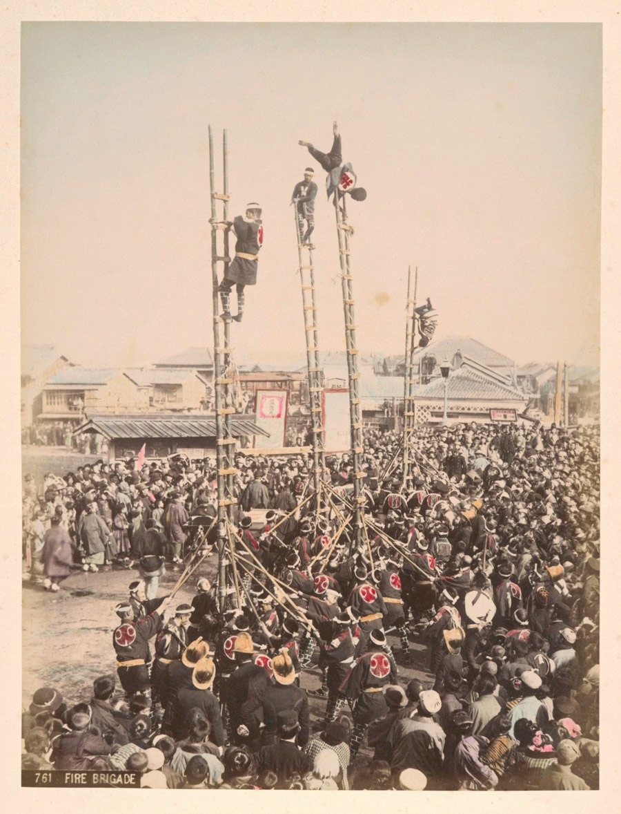 أعضاء من فرقة الإطفاء يتنافسون على صعود السلالم الخشبية تعلو إلى السماء ويقومون بأعمال استعراضية أمام حشود من الناس حوالي سنة 1890