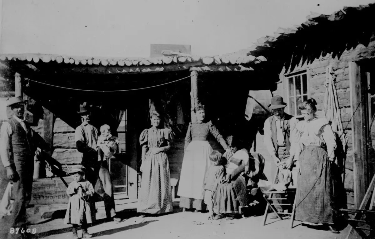 عائلة خارج منزلها، مع امرأة أمريكية أصلية تعمل كخادمة لديها وتحمل طفلها في (نيو ميكسيكو) سنة 1895.