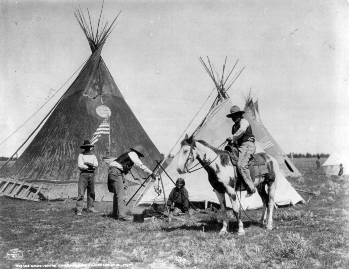 صورة سنة 1906 لرجال يمتطون الخيول توقفوا عند «محمية حصن بيلكناب» للأمريكيين الأصليين في (مونتانا)، يتم في هذه الصورة شواء كلب فوق النار.