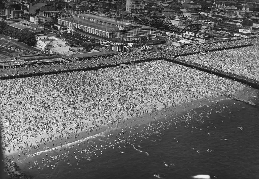 صورة لحشد غفير من الناس وهم يقضون وقتاً ممتعاً ويتمشون على شاطئ وممشى (كوني آيلاند) الخشبي، و(كوني آيلاند) هي شبه جزيرة في جنوب مدينة (نيويورك). في الرابع من يوليو عام 1946