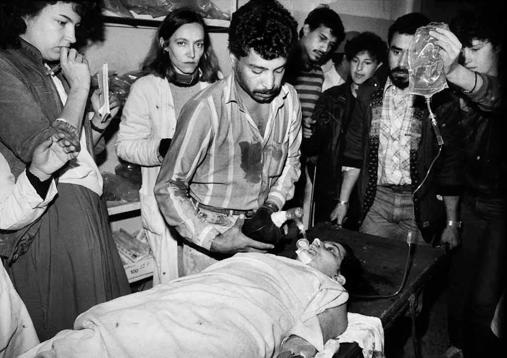 (ماري كولفين) عندما كانت شابة يافعة على أقصى اليسار، داخل مخيم اللاجئين برج البراجنة بالقرب من بيروت في لبنان سنة 1987، تشاهد بينما يكافح أحد زملائها من أجل إنقاذ حياة أحد اللاجئين.