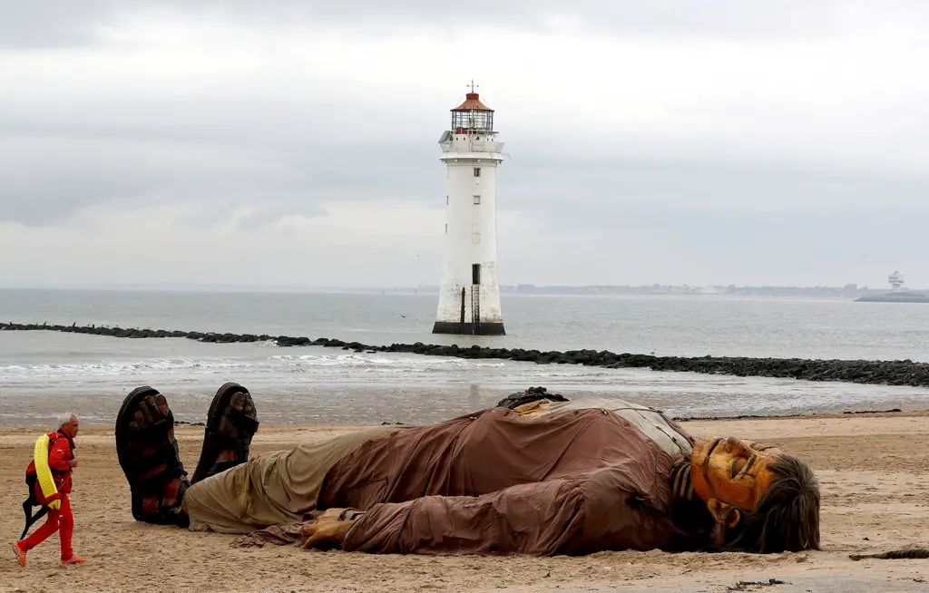 أحد حراس الشواطئ يمر بالقرب من دمية متحركة عملاقة مستلقية على شاطئ 