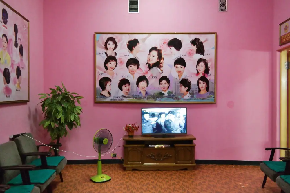 غرفة زهرية اللون مع مقاعد وصور لتصفيفات شعر نسائية