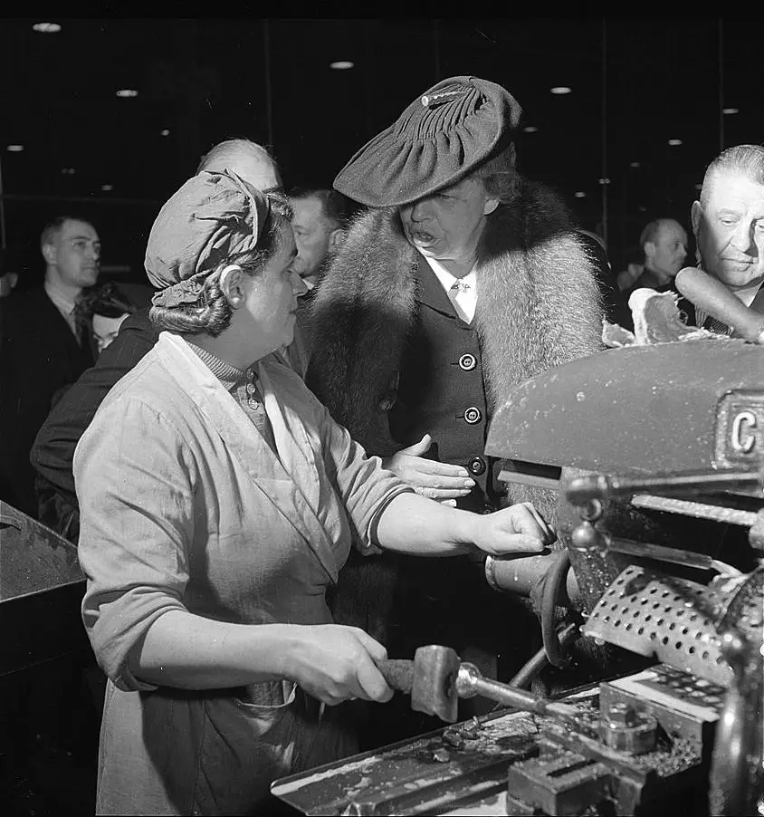 امرأة تعمل على تسيير إحدى الآلات تتحدث إلى السيدة الأولى الأمريكية (إيليونور روزفلت) خلال جولتها التي طافت بريطانيا العظمى سنة 1942.
