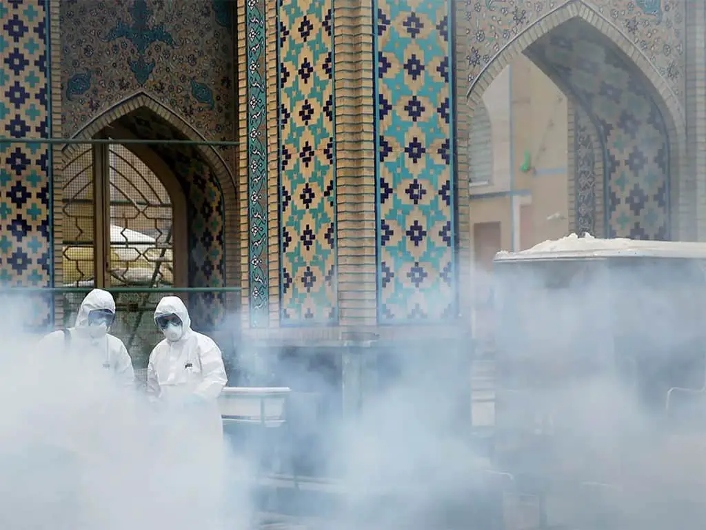 أفراد فريق طبي يرشون المواد المطهرة لتعقيم المنطقة الخارجية لمقام الإمام رضا المقدس في إيران.