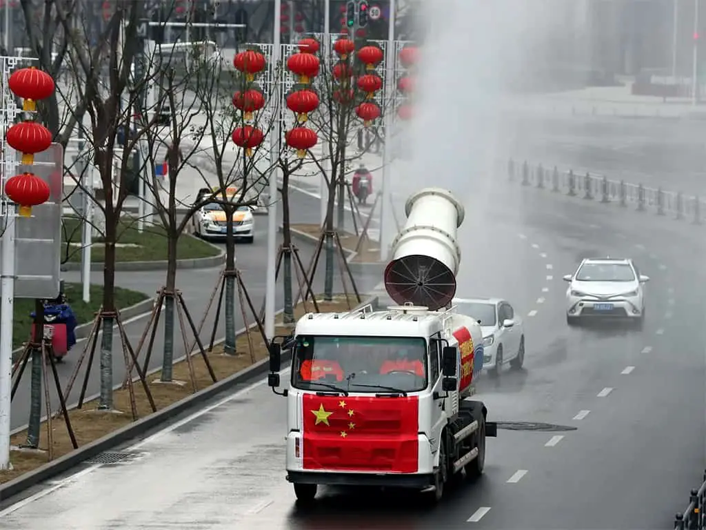 عمال يشغلون عربة تحمل بخاخة صناعية لتعقيم الشارع في الصين.
