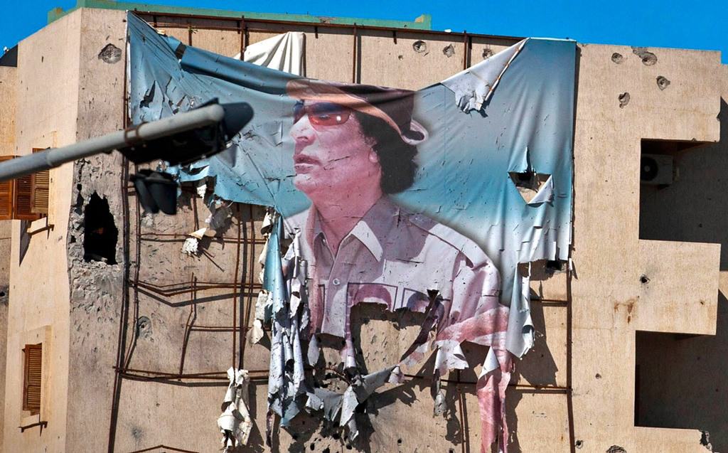 لافتة ممزقة لمعمر القذافي معلقة من مبنى خلال معركة في وسط مدينة سرت في 12 أكتوبر 2011، قبل ثمانية أيام من وفاته. صورة: Majid Saeedi/Getty Images